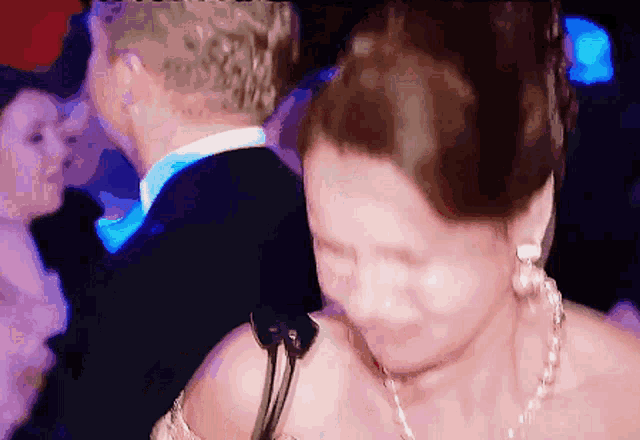 a woman wearing a necklace and earrings is dancing with a man in a tuxedo