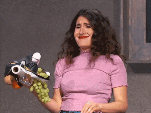 a woman in a pink shirt is holding a bunch of grapes and a bottle