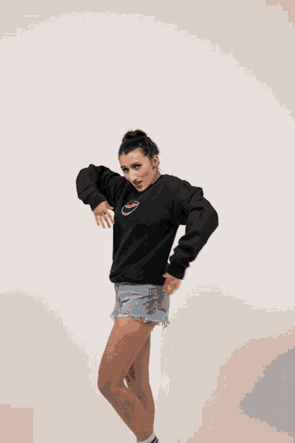 a woman wearing a black sweatshirt and denim shorts is making a funny face