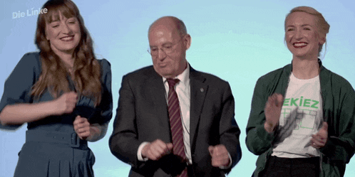 a man in a suit and tie is dancing with two women wearing a shirt that says " ekiez "