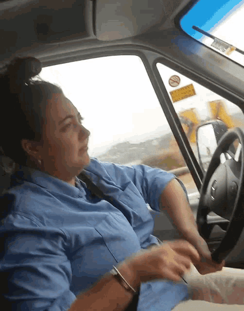a woman in a blue shirt is driving a car with a no smoking sticker on the windshield