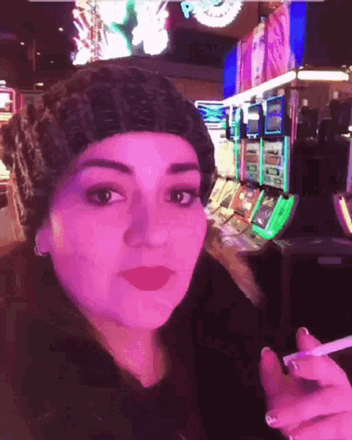 a woman in a beanie is smoking a cigarette in front of a slot machine