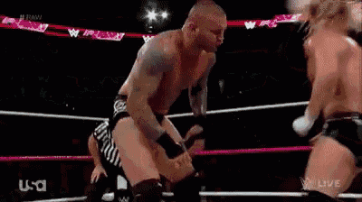 two men are wrestling in a ring with a referee in the background .