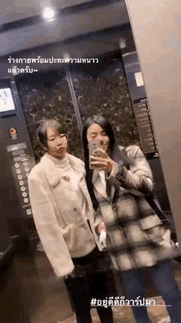 two women are taking a picture of themselves in an elevator with a phone .