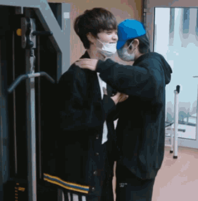 a man wearing a blue hat is hugging another man wearing a face mask