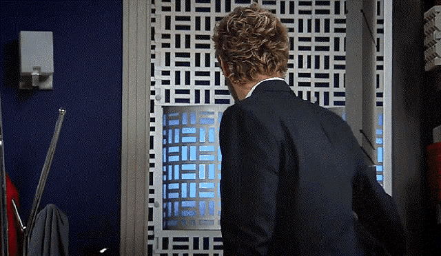 a man in a suit stands in front of a wall that has a geometric pattern