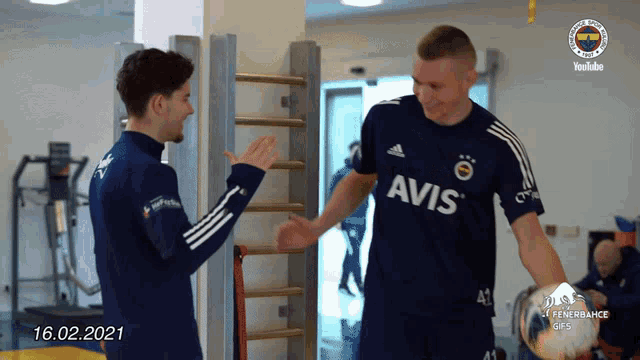 a man wearing an avis shirt shakes hands with another man in a gym