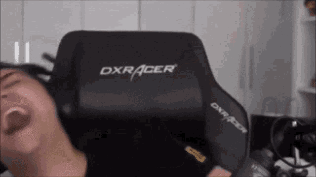 a man is sitting in a black dxracer chair with his mouth open .