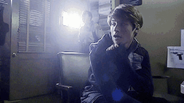a young boy is sitting in a chair in a dark room with a picture of a gun on the wall
