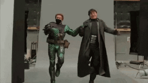 a man in a green costume and a man in a black coat are dancing together in a room .