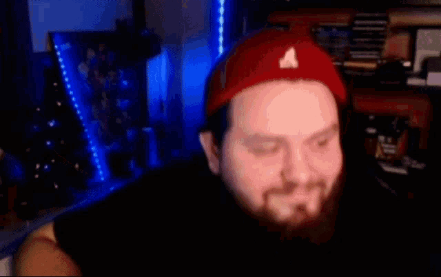 a man with a beard wearing a red hat is standing in front of a blue light .
