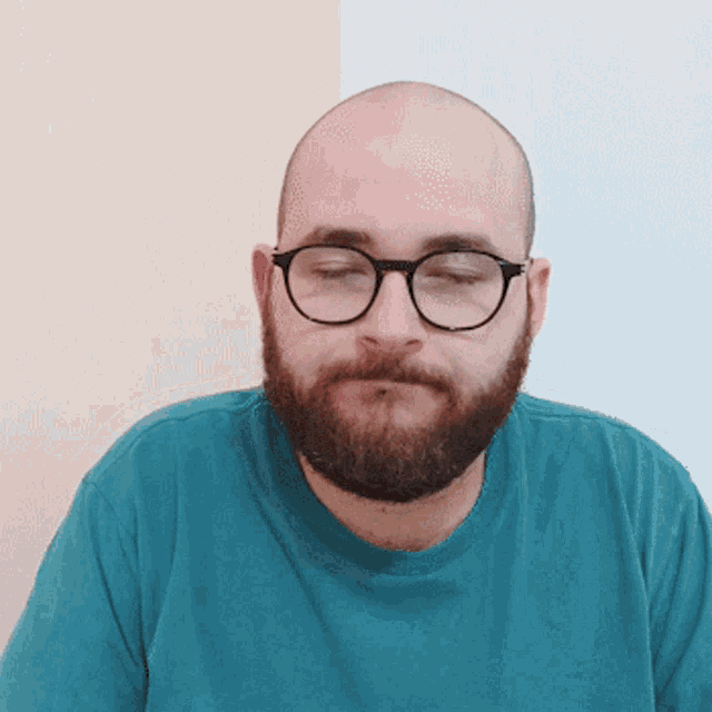 a bald man with a beard wearing glasses and a teal shirt