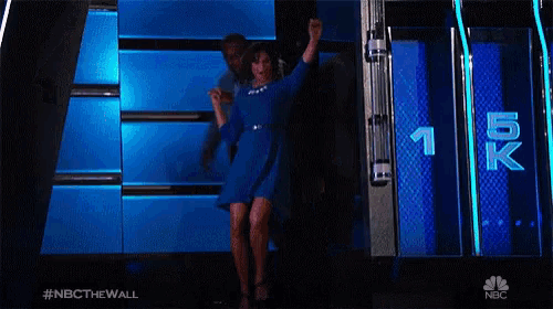 a woman in a blue dress is jumping in the air while a man watches