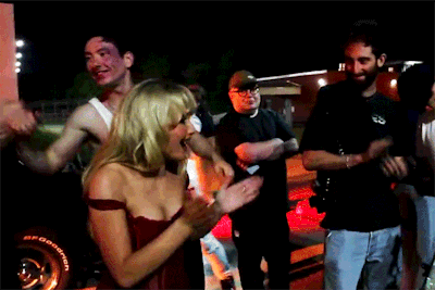 a woman in a red dress is standing next to a man with a bfgoodrich tire on his car