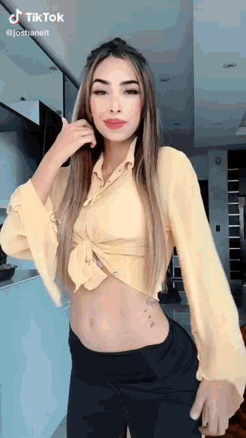 a woman wearing a yellow crop top and black pants is standing in a kitchen .
