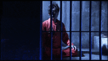a man in a red jumpsuit is sitting in a jail cell behind bars