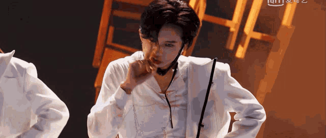 a man in a white suit with a microphone around his neck stands on a stage