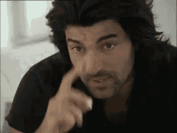 a man with long hair and a beard is touching his face with his hand .