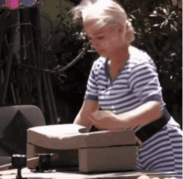 a woman in a blue and white striped shirt is working on a piece of wood