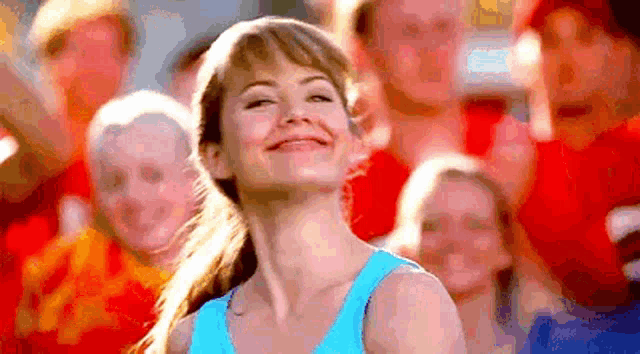 a woman in a blue tank top is smiling in front of a crowd .