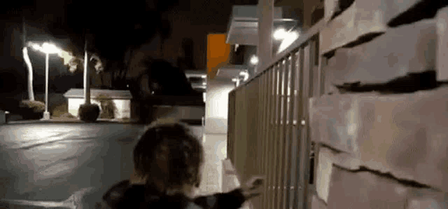 a person is walking down a sidewalk at night in front of a brick wall .