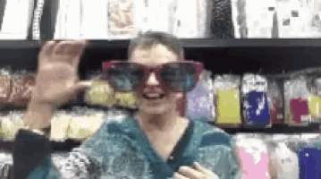 a woman wearing a pair of large sunglasses is standing in front of a shelf .