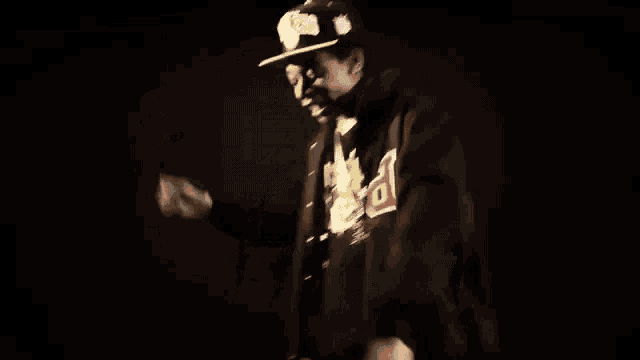 a man wearing a hat and a hoodie is dancing in the dark .