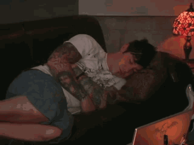 a man with tattoos is sleeping on a couch with a lamp in the background