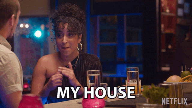 a woman is sitting at a table with a man and says " my house "