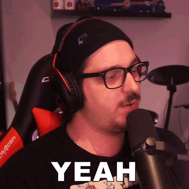 a man wearing headphones and glasses says " yeah " in front of a microphone