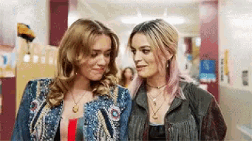 two women are standing next to each other in a hallway and smiling .