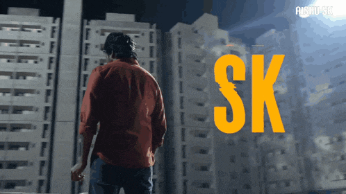 a man in a red shirt is standing in front of tall buildings and the word sk is visible