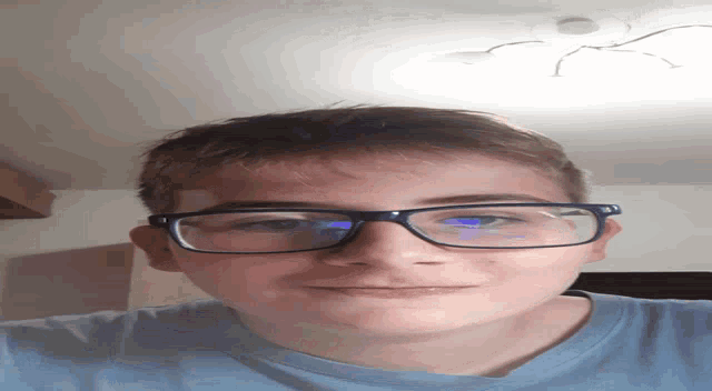 a young man wearing glasses and a blue shirt looks down at the camera