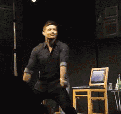 a man in a black shirt is standing on a stage in front of a chair