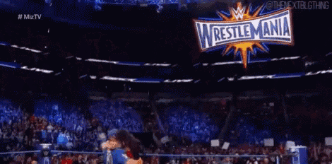 a wrestler is carrying a woman in his arms in a wrestling ring .