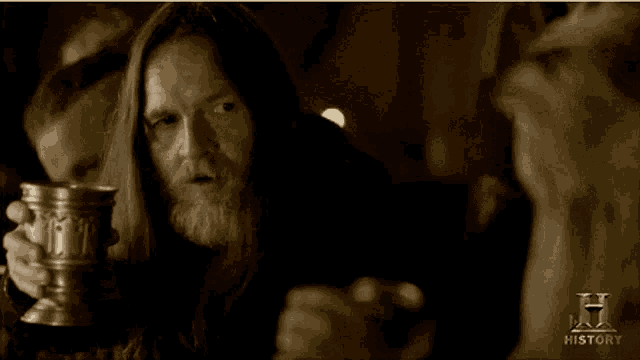 a man with long hair and a beard is holding a cup with the word history written on it