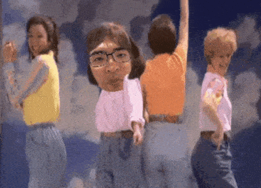 a group of women are dancing in front of a blue sky with a man with glasses on his head .
