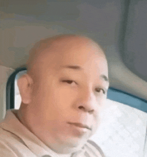 a bald man is sitting in the back seat of a car and looking at the camera .