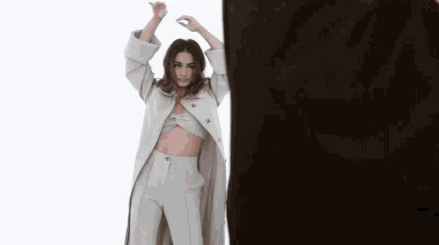 a woman in a trench coat and crop top is standing in front of a white background