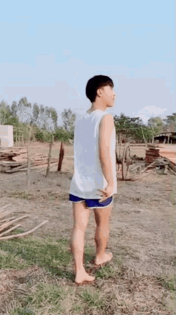 a young man in a white tank top and blue shorts is standing on a grassy field .