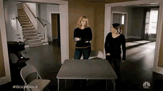 two women are standing next to a folding table in a room .