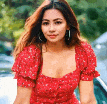 a woman in a red dress and hoop earrings is standing in front of a car