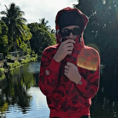 a man in a red hoodie and sunglasses is standing next to a river .
