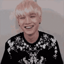 a young man with blonde hair is smiling while wearing a black sweater with white flowers on it .