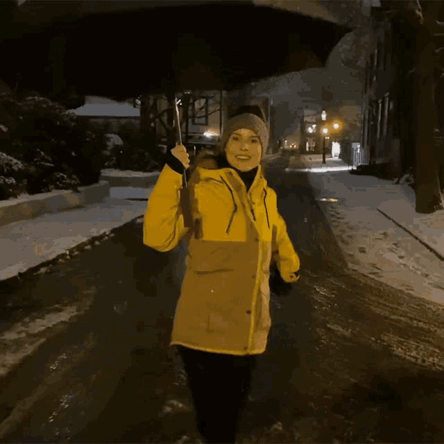 a woman in a yellow jacket is holding an umbrella on a snowy street