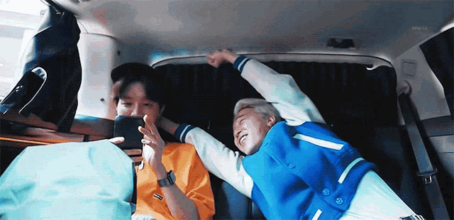 two men are laying in the back of a car playing a game on a cell phone .