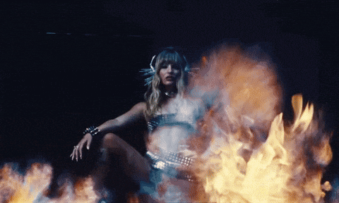 a woman is sitting in front of a fire in a dark room