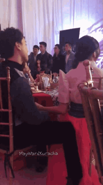 a group of people sitting at a table with maywardkuracha written on the bottom right