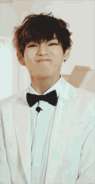 a young man in a white suit and black bow tie makes a face