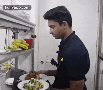 a man is standing in a kitchen with plates of food on a counter .